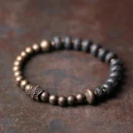 Lava rock and copper beaded Buddhist bracelet with black porous beads and bronze metal accents on rustic brown surface