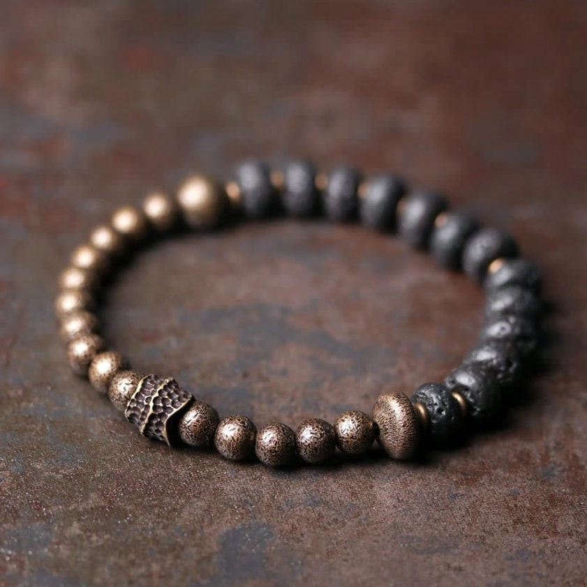 Lava rock and copper beaded Buddhist bracelet with black porous beads and bronze metal accents on rustic brown surface