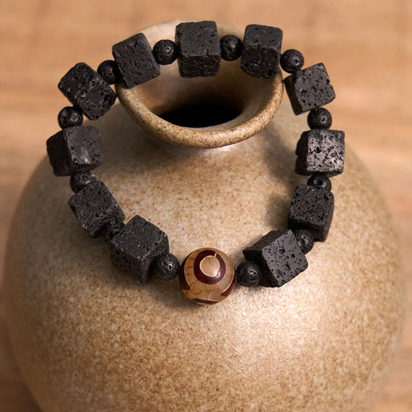 Overhead flat lay of lava rock and three-eyed dzi bead bracelet arranged around ceramic vase on tabletop