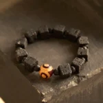 Lava rock and three-eyed dzi bead healing bracelet with square black volcanic stone beads arranged on wooden surface