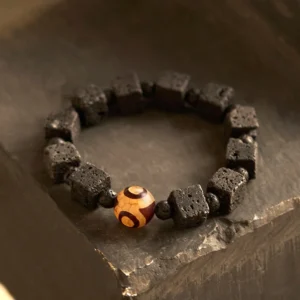 Lava rock and three-eyed dzi bead healing bracelet with square black volcanic stone beads arranged on wooden surface