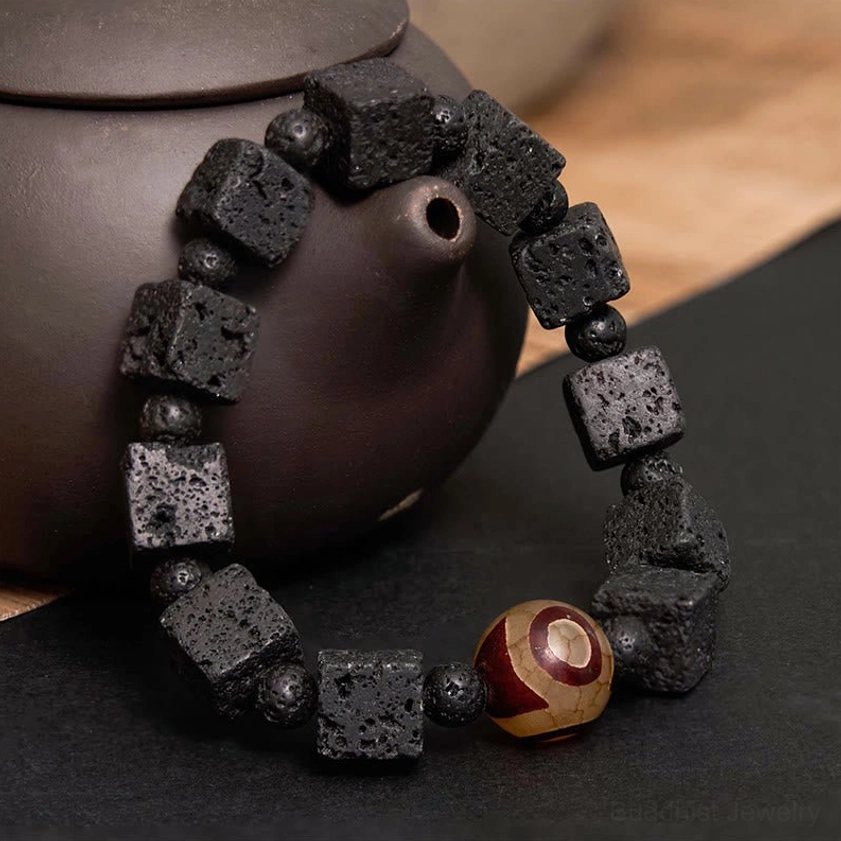 Close-up side view of lava rock dzi bead protection bracelet draped over traditional clay teapot showing bead texture