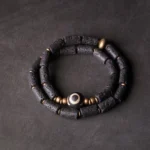 Three-eye Dzi bead lava rock wrap bracelet with brass accents flat lay view