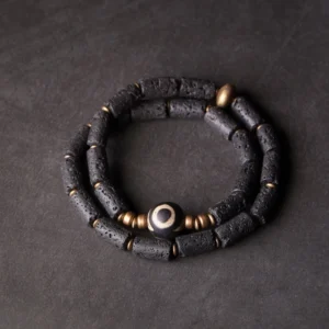 Three-eye Dzi bead lava rock wrap bracelet with brass accents flat lay view