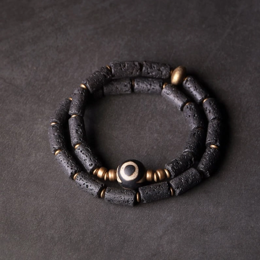 Three-eye Dzi bead lava rock wrap bracelet with brass accents flat lay view
