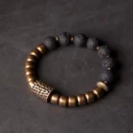 Lava rock and brass healing bracelet with rainbow obsidian beads, top-down full view on dark background showing complete bead arrangement