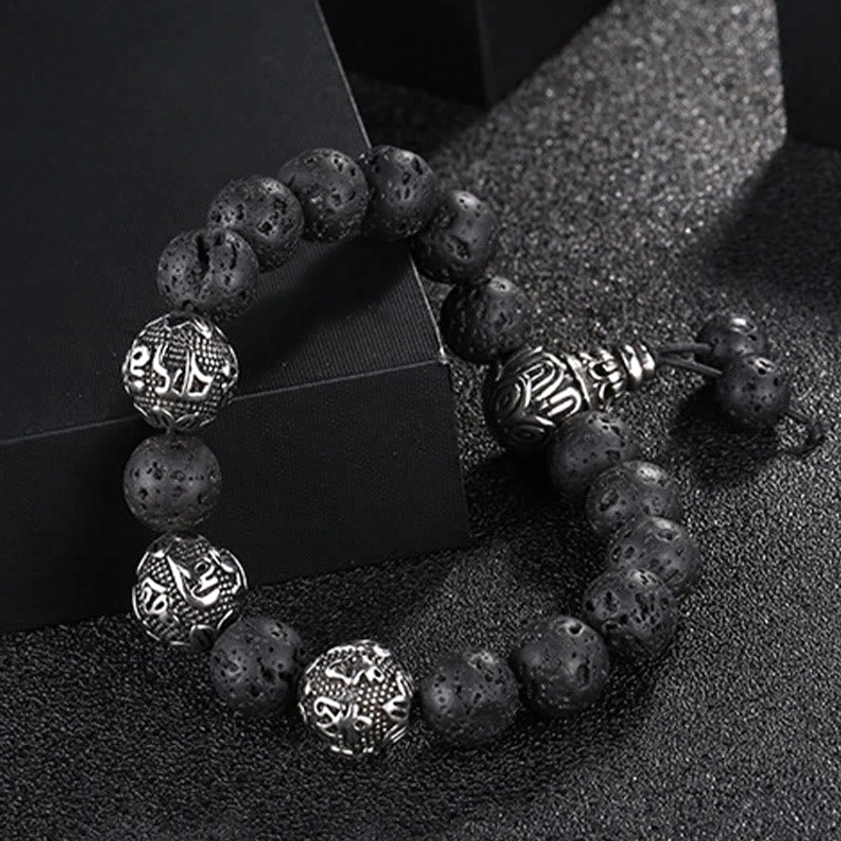 Lava rock and black obsidian Buddhist bracelet with engraved titanium steel mantra beads on black textured background