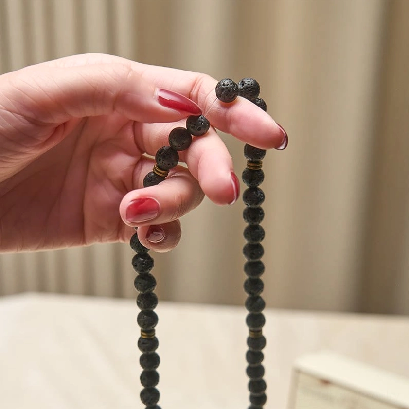 Two authentic lava rock prayer bead mala strands held in hand with bronze spacer details and lotus pendants