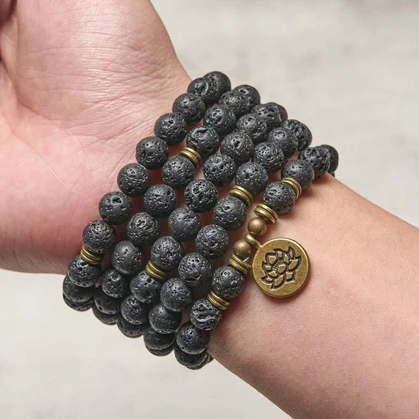 Lava rock wrap mala bracelet worn on wrist showing multi-wrap design with bronze lotus charm and porous bead texture