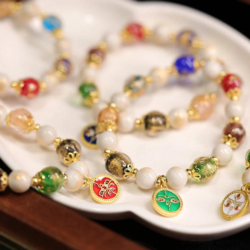 Layered Five Gods of Wealth Buddhist bracelets with multiple enamel deity charms and colorful liuli glass beads on porcelain