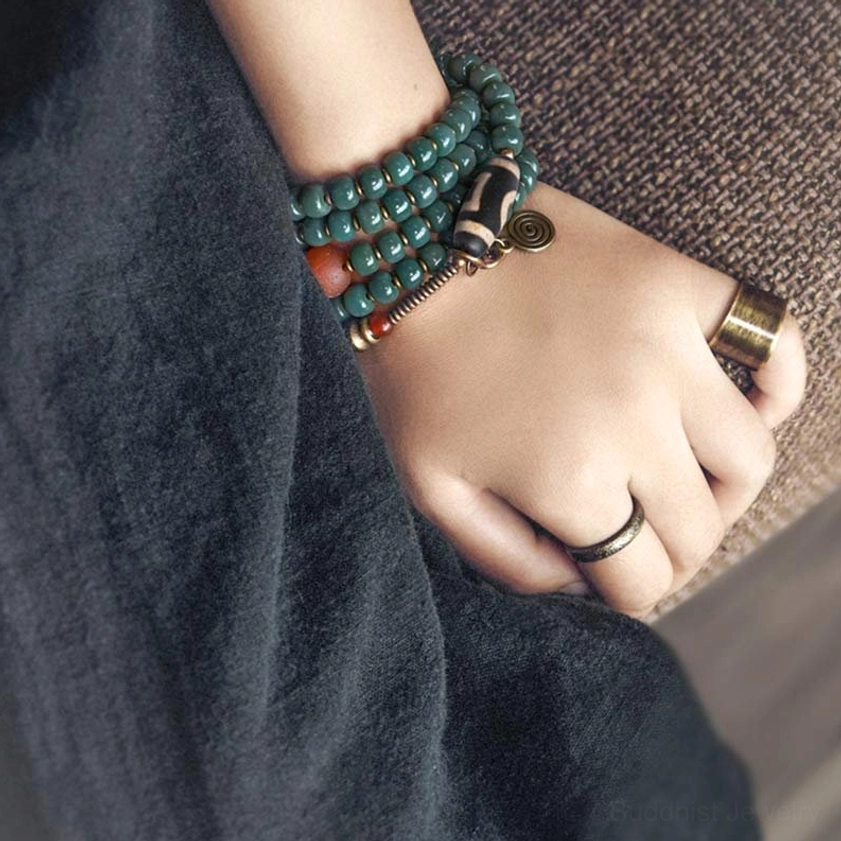 Multi-layer Buddhist mala bracelets stacked on wrist with teal bodhi beads, dzi bead accents, and vintage metal rings