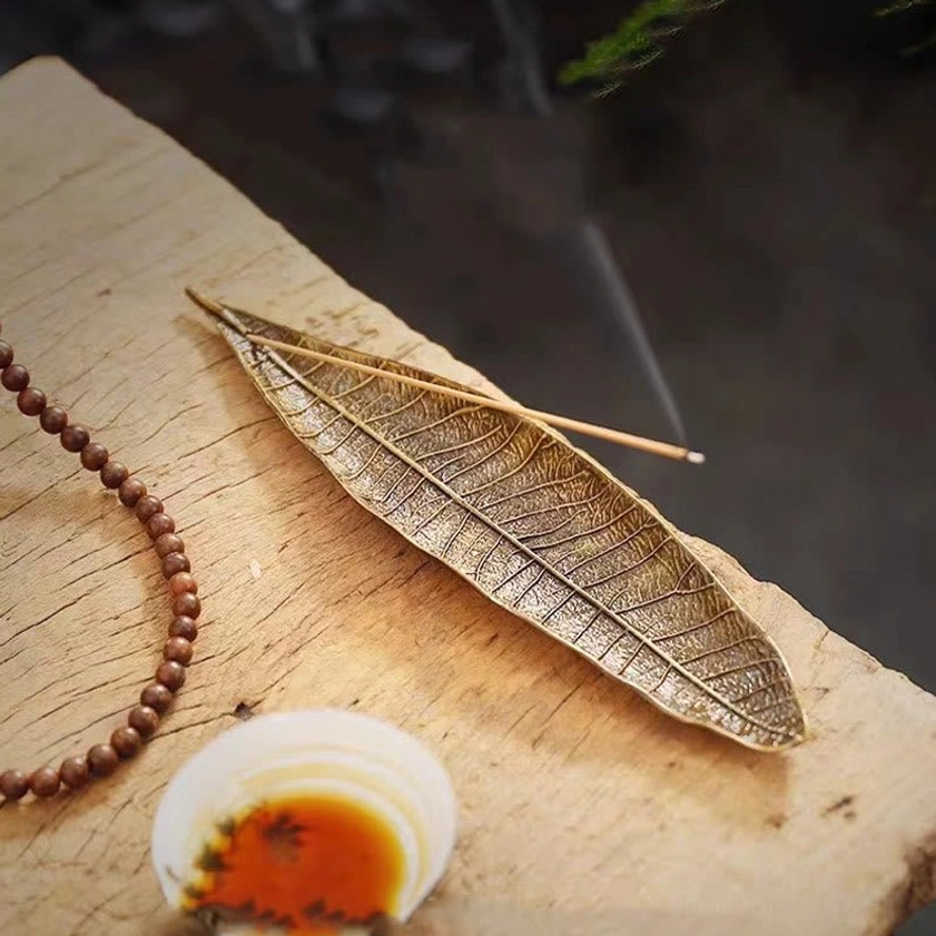 Buddhist leaf incense burner with lit stick and rising fragrant smoke showing detailed leaf veins on tea table