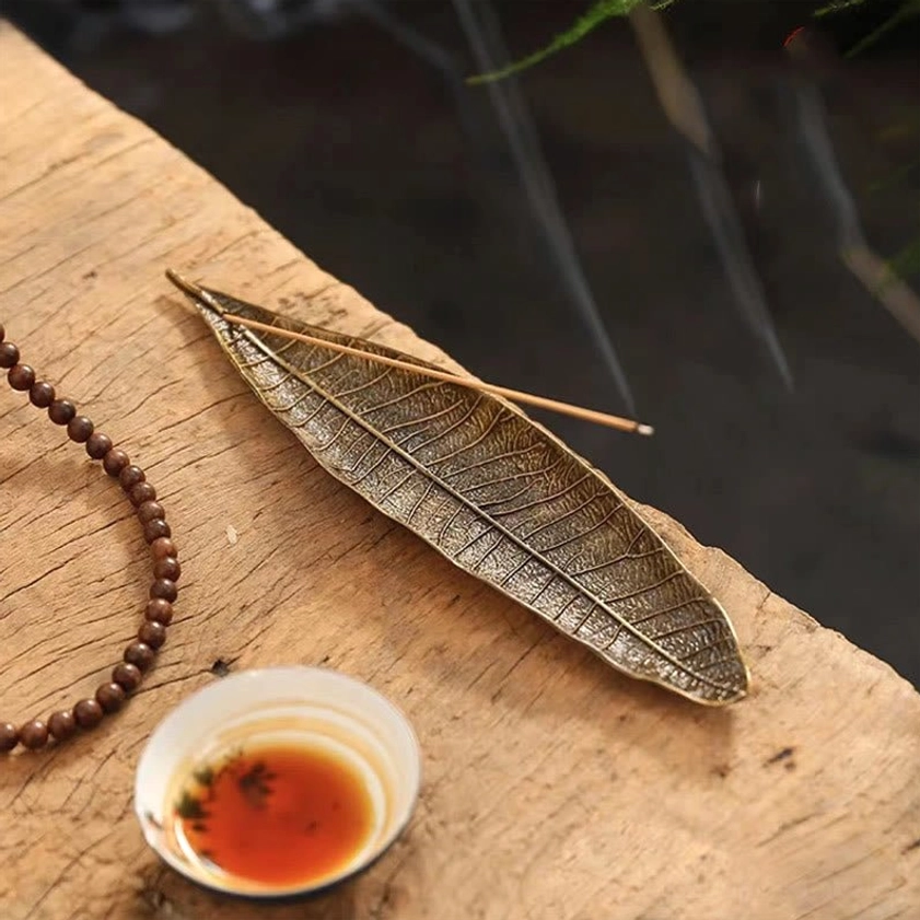Buddhist leaf incense burner with lit incense and rising smoke on tea table with cup and prayer beads