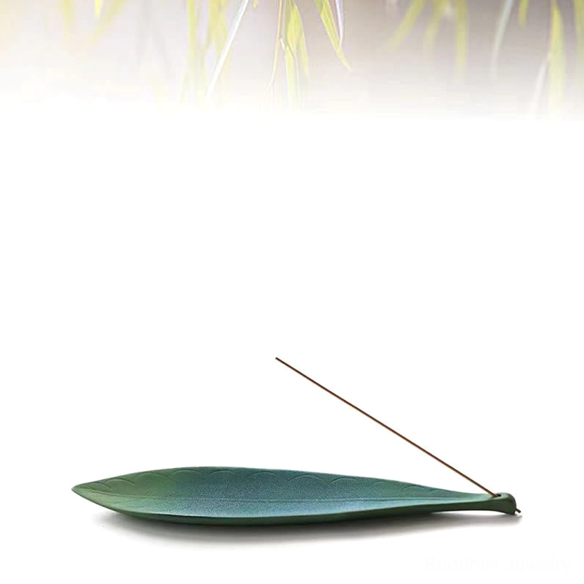 Dark teal ceramic leaf incense holder with single incense stick on white background