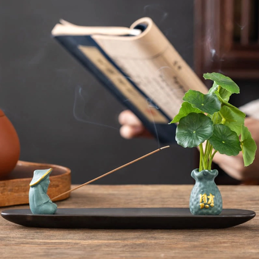 Light blue Fisherman ceramic incense burner beside books and tea set in meditation space side view with lit incense
