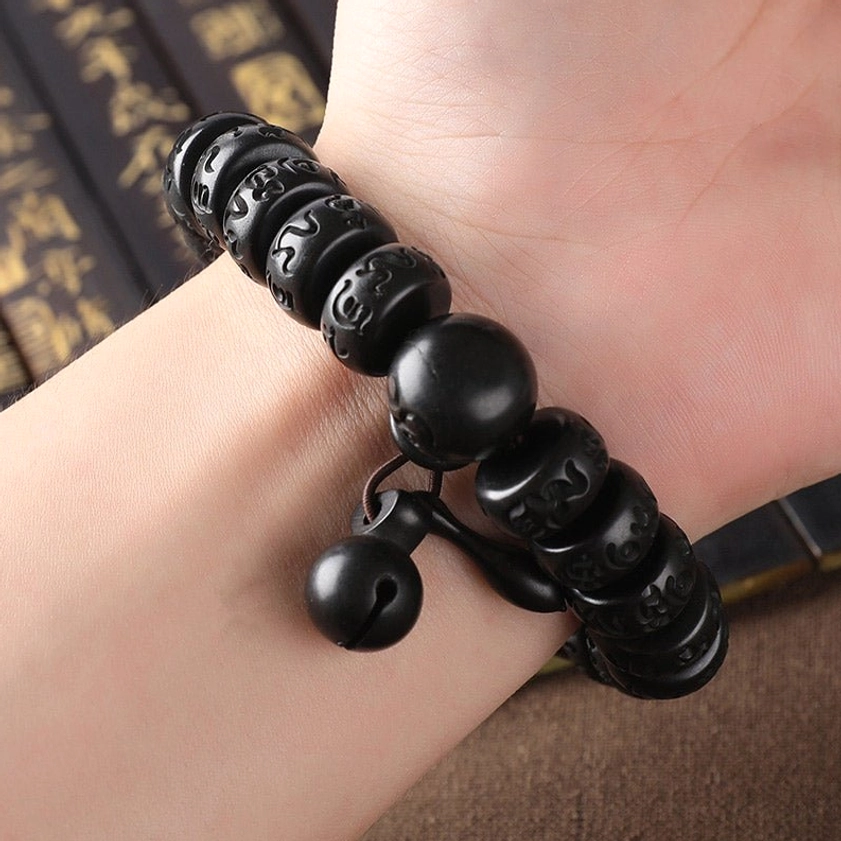 Buddhist wooden protection bracelet worn on human wrist, showing fit and carved black mantra beads with dual bell pendants