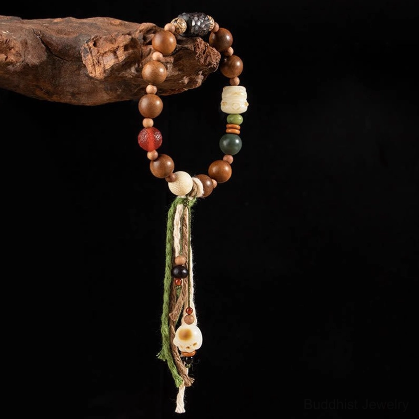 Vertical hanging view of handmade Buddhist bracelet with carved cat paw pendant and long flowing tassel against black background