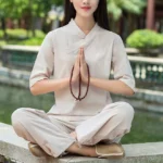 Light khaki linen meditation and tai chi two-piece set with V-neck top and relaxed pants, flat lay view in traditional garden setting