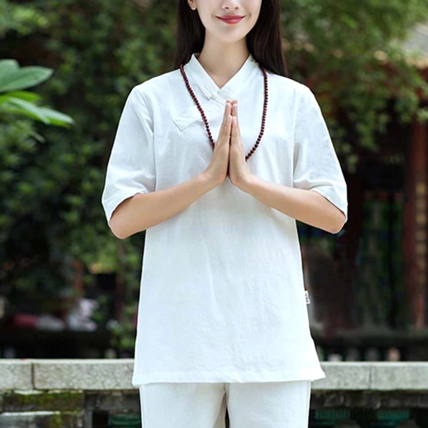 Woman in white linen meditation outfit with cross collar and half sleeves wearing prayer beads, practicing Tai Chi in garden