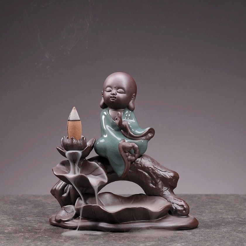 Little monk ceramic backflow incense burner with lotus holder, front three-quarter view, brown ceramic base with celadon robes, indoor tabletop display with flowing smoke effect