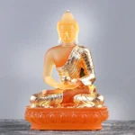 Handcrafted amber Liuli glass Buddha statue with gold plating in meditation pose holding ritual bowl, front view on gray background