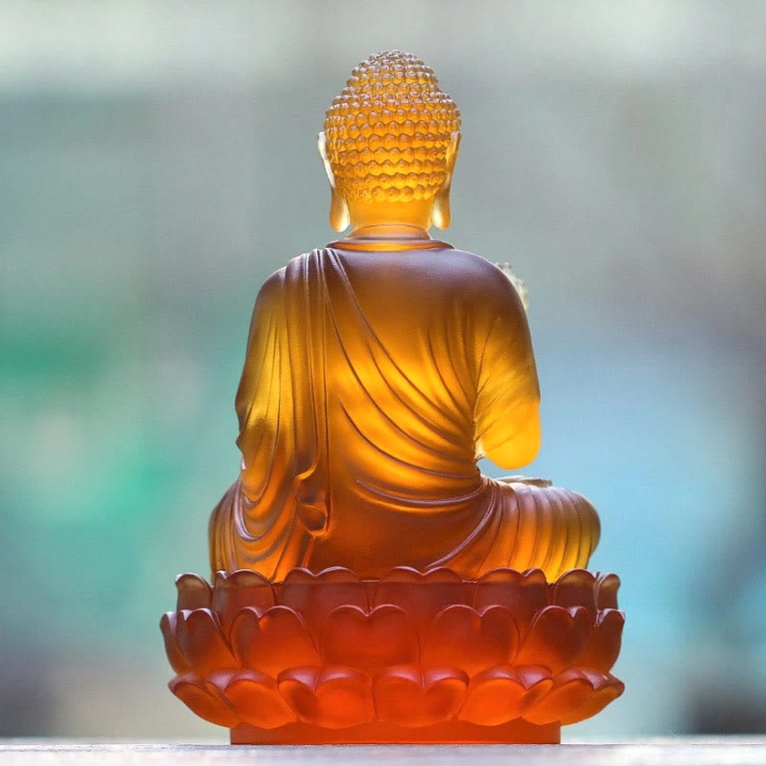 Sakyamuni Buddha statue rear view with translucent amber glass showing back robe details, topknot, and lotus base