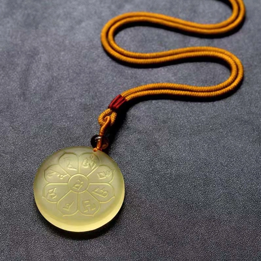 Buddhist wealth mantra necklace flat lay overhead showing braided rope with red-brown decorative elements and light yellow pendant