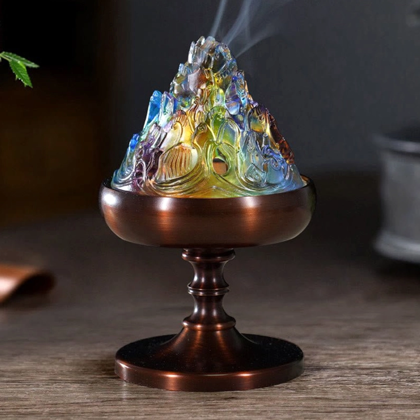 Liuli crystal mountain incense burner with bronze pedestal and multicolor glass lid releasing aromatic smoke on wooden table