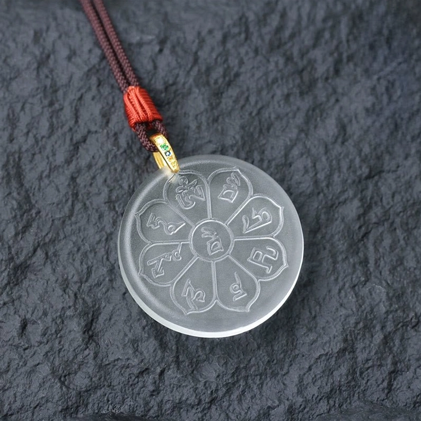 White translucent Liuli crystal eight-petal mantra pendant necklace with dark rope, gold clasp and gem accent on rock background