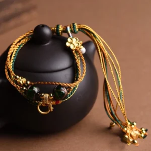 Handmade liuli glass bead braided bracelet with gold and teal woven cord, dark green glass beads, and four-leaf clover charm for protection and balance