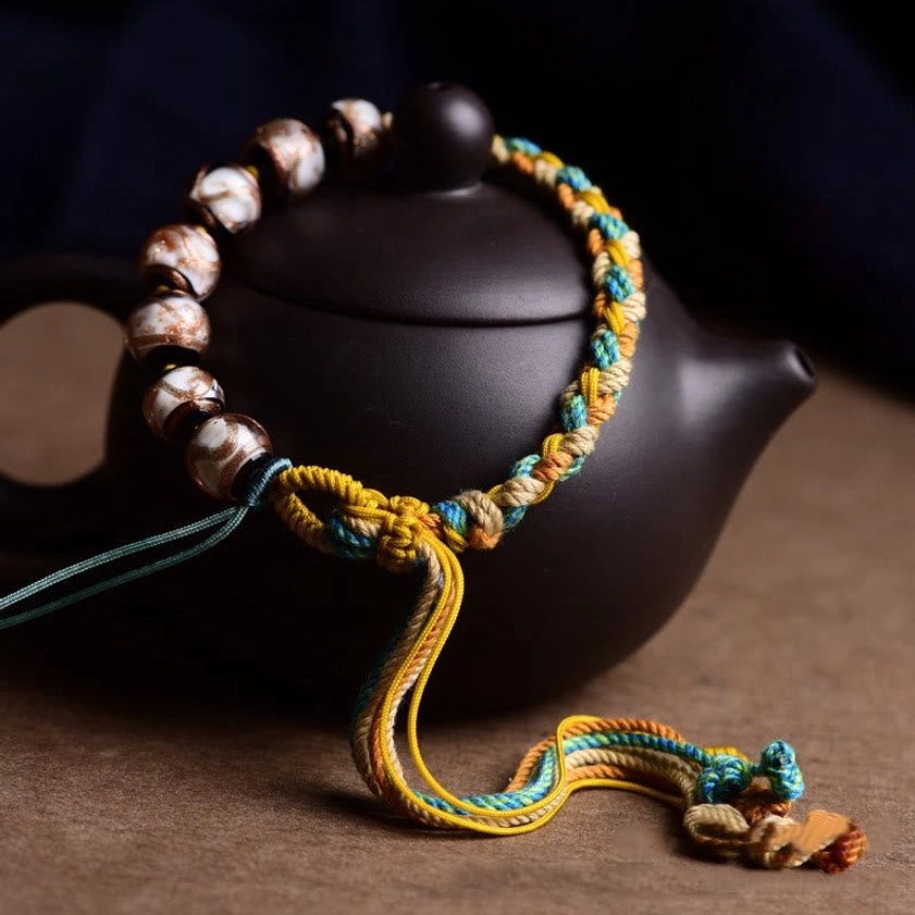 Buddhist fortune bracelet with woven rope and brown-toned glass beads displayed on ceramic teapot