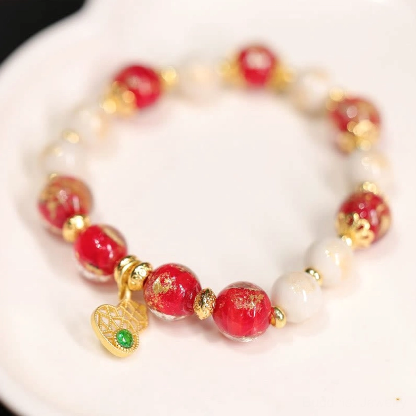 Buddhist gourd charm bracelet with red and white beads, gold-flecked Liuli glass, and green stone pendant on white ceramic display