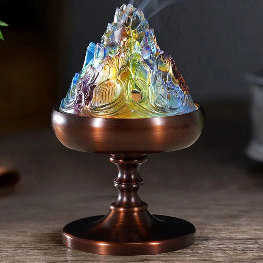 Low-angle view of complete Liuli crystal mountain incense burner with bronze pedestal and rising incense smoke