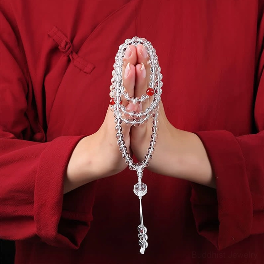 Buddhist 108 bead prayer mala held in hands, close-up view showing red spacer beads and crystal tassel pendant