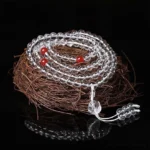 Red beads white string 108 bead Buddhist prayer mala with crystal tassel, overhead angled view on textured background