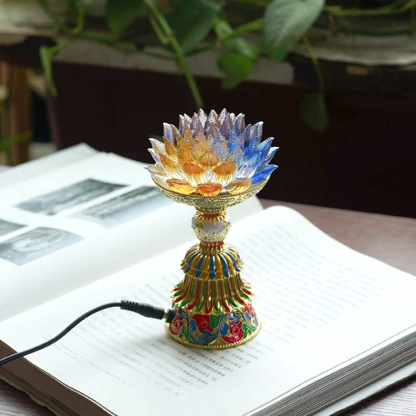 Handcrafted liuli glass lotus lamp with gradient petals connected to USB charging cable on open book