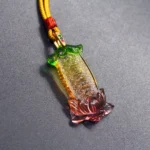 Om Mani Padme Hum Liuli lotus pendant necklace with gradient green amber red glaze and engraved sacred mantra text, overhead flat lay view