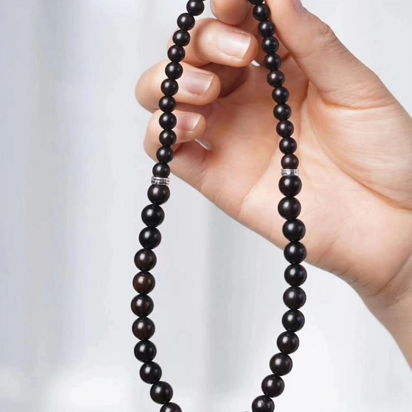 Long wooden dzi bead necklace with dark ebony beads and metal accents held by hand close-up side view against gray background