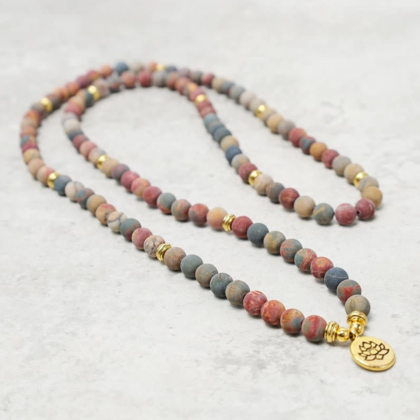 Long prayer bead mala with mixed stone beads and golden accents featuring lotus metal charm pendant, flat lay overhead shot