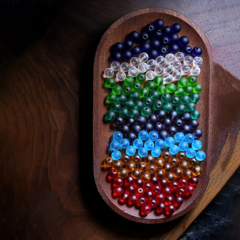 Loose sorted multicolored Liuli glass mala beads arranged in gradient on wooden tray, showing full spectrum of frosted bead colors