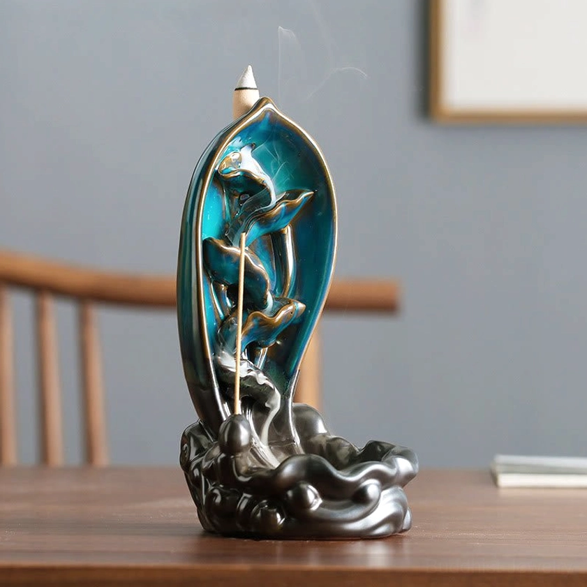Lotus-themed backflow incense burner with blue glazed interior and dark brown wave ceramic base, displayed on wooden desk with stick incense
