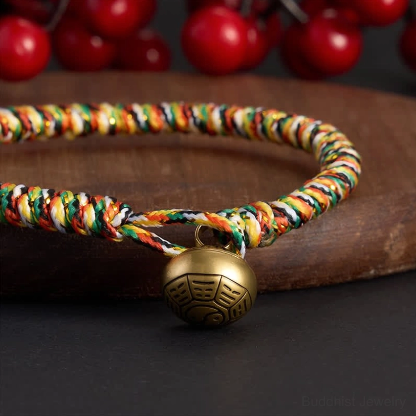 Close-up detail of twisted braided cord and brass bagua bell pendant on multicolor Buddhist balance bracelet