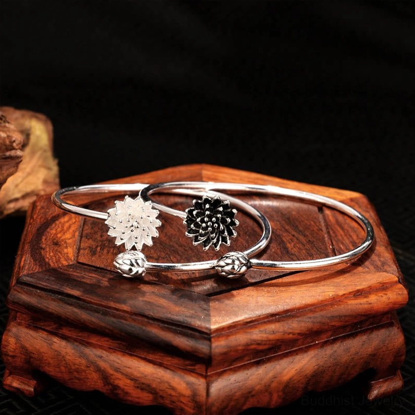 Two Buddhist lotus bangles - silver and gray styles displayed together, top-down view on wooden jewelry stand