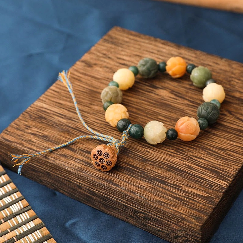 Close-up detail of hand-carved lotus bead on Buddhist bracelet with multi-color stone beads on bamboo mat background