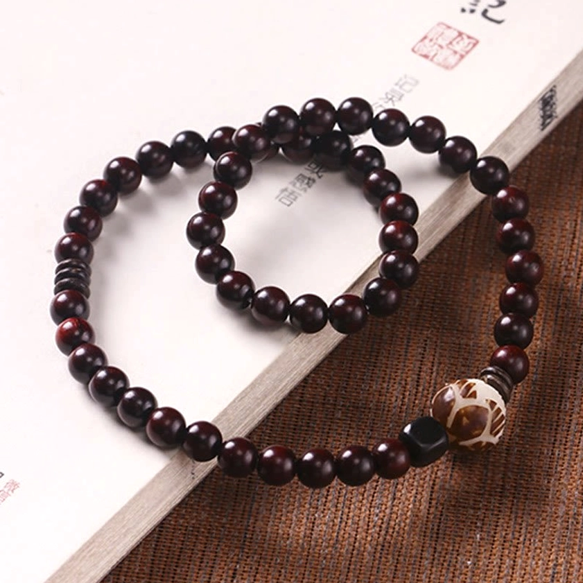 Double wrap beaded bracelet on hardcover book surface, highlighting dark brown red sandalwood beads with hand-carved lotus focal bead