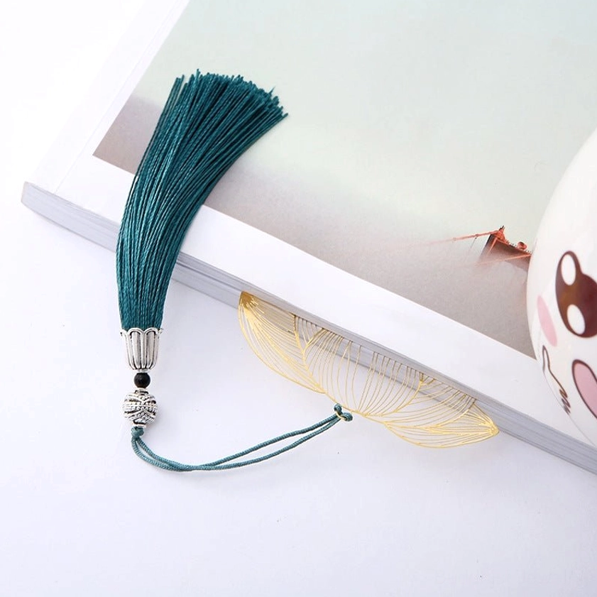 Lotus brass bookmark flat lay on open book - gold hollow lotus design with teal tassel and silver ornaments