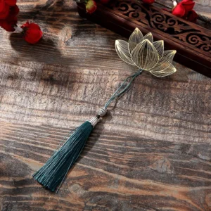 Lotus flower brass hollow bookmark with teal tassel on vintage wooden desk - elevated oblique view showing intricate carved gold design