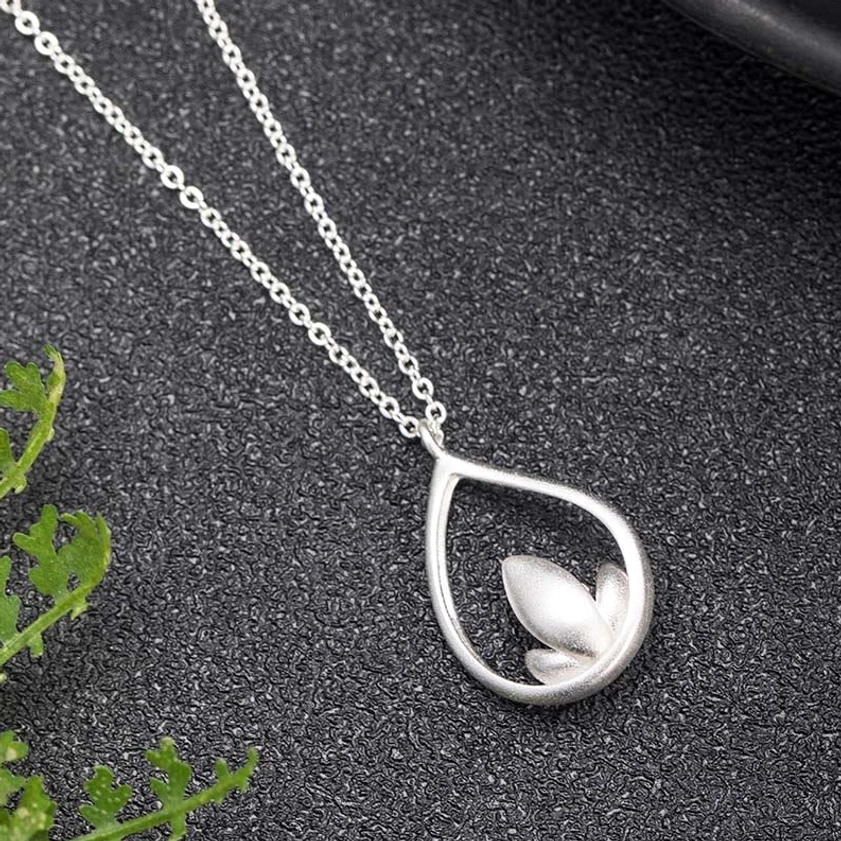 Enlightenment lotus silver pendant necklace showing closed lotus bud design in teardrop frame, three-quarter front angle on dark foliage backdrop