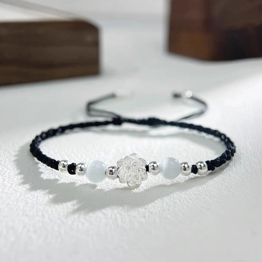Sterling silver lotus cat's eye protection bracelet with black braided cord on wooden surface - close-up flat lay
