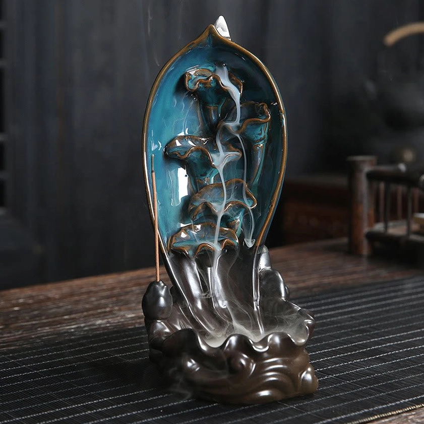 Lotus style backflow incense holder with teal glazed interior showing flowing cascading incense smoke effect on dark wooden table